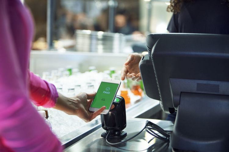 Cropped image of customer paying bill thought smart phone in restaurant