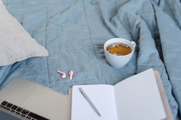 A scene in pastel colors laptop, notepad, and a cup of herbal tea on the bed.