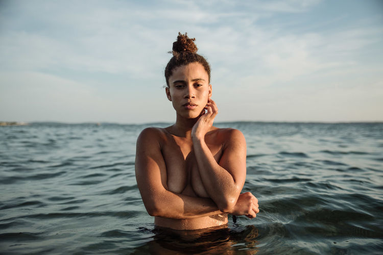 Portrait of shirtless woman in sea against sky during sunset