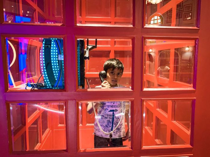 Portrait of boy talking while standing in illuminated telephone booth