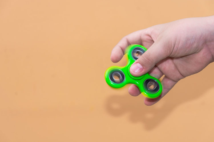 Cropped hand holding fidget spinner against brown background