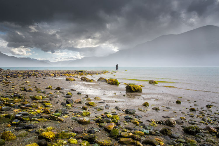 Mid distance of person standing in sea against cloudy sky