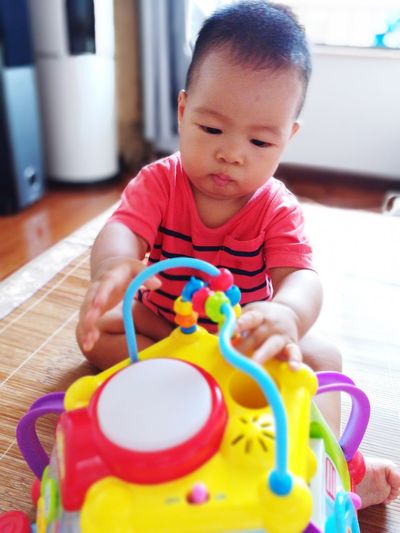 Close-up of cute baby boy playing with toys while sitting on mat at home