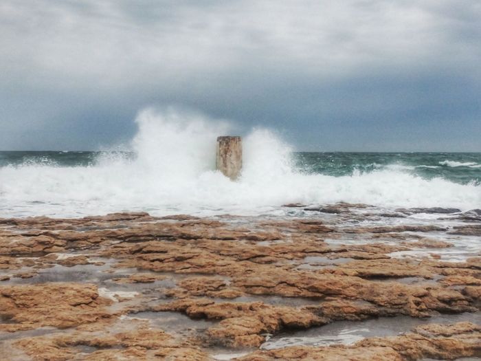 Waves breaking on rocks against sky