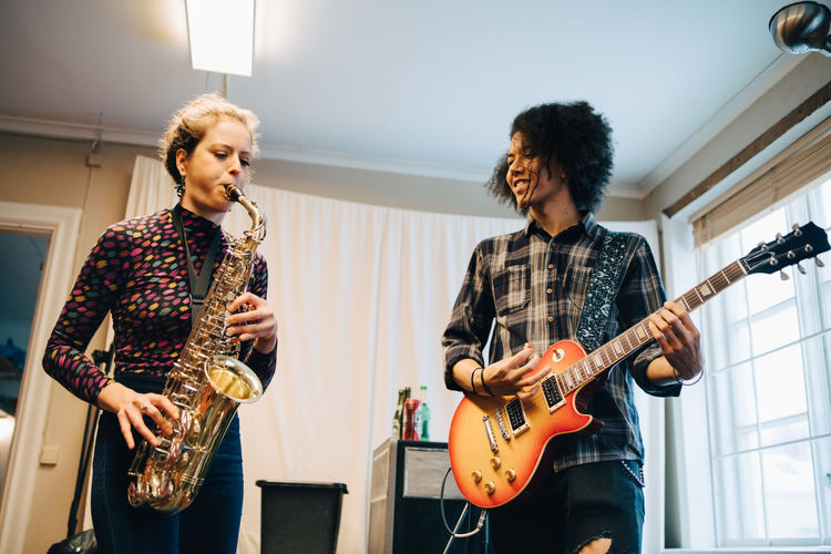 Friends playing saxophone and guitar while practicing at recording studio