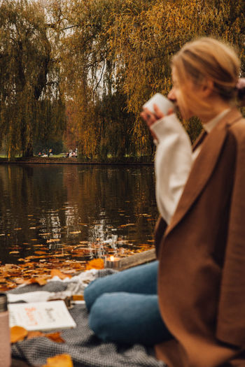Rear view of woman sitting by lake during autumn