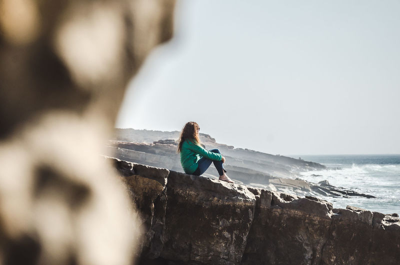 People on rock at beach against sky