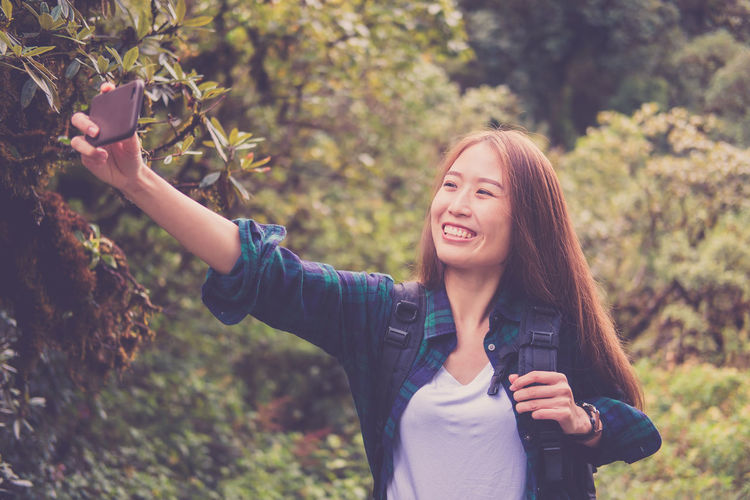 Portrait of a smiling young woman standing against trees