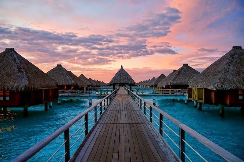 Empty pier and stilt houses on lagoon against sky during sunset at bora bora