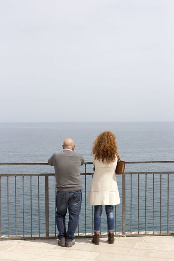 Rear view of man and woman standing at observation point by sea against sky