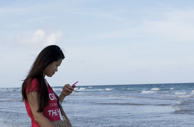 Side view of young woman using mobile phone in sea