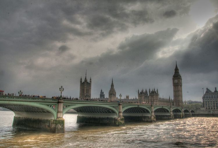 Westminster bridge over thames river against cloudy sky