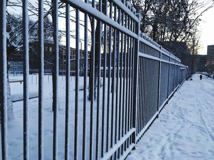Snow covered railing by fence during winter