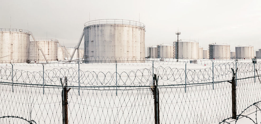 Fuel storage tanks in winter, tank farm behind a fence topped with barbed wire