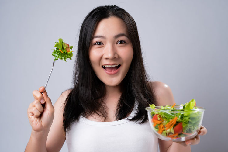 Portrait of smiling woman holding food against gray background