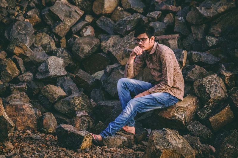 Thoughtful young man looking away while sitting on rock