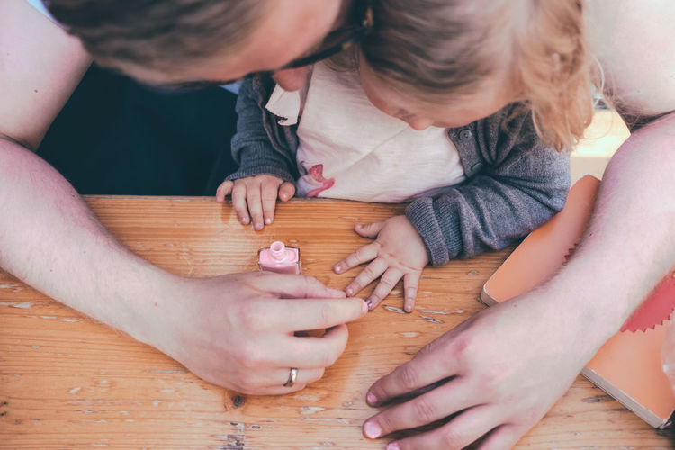 High angle view of father painting daughter fingernails on table outdoors