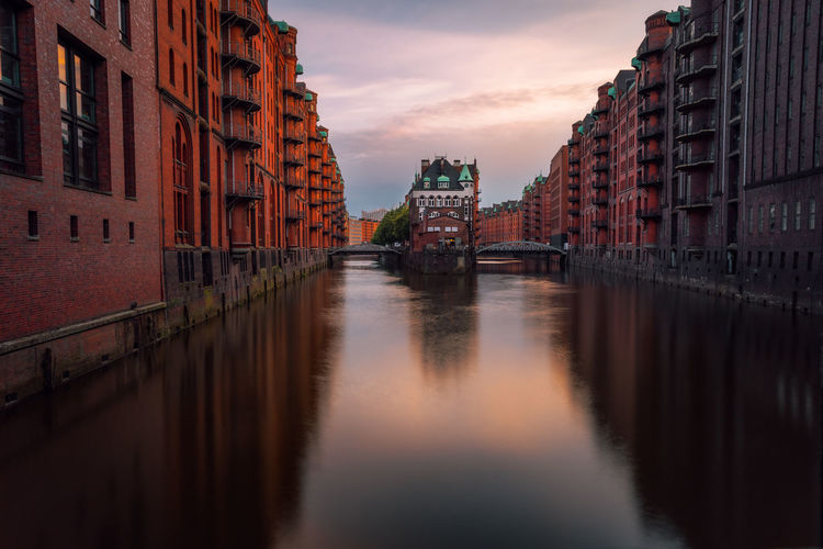 Canal amidst buildings in city against sky during sunset