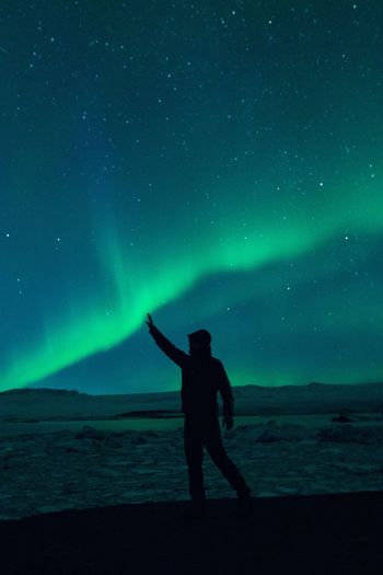 Optical illusion of silhouette man touching aurora borealis in sky