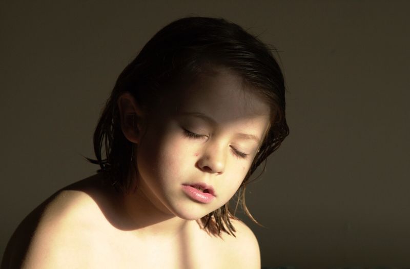 Close-up of shirtless girl with eyes closed against beige background