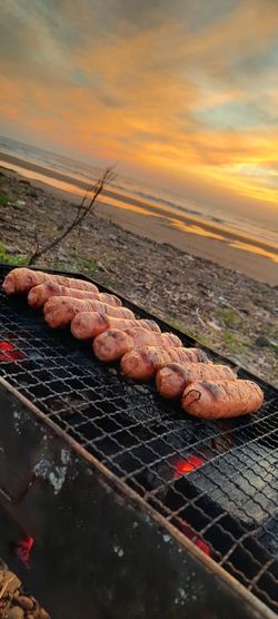 Close-up of meat on barbecue grill against sky during sunset