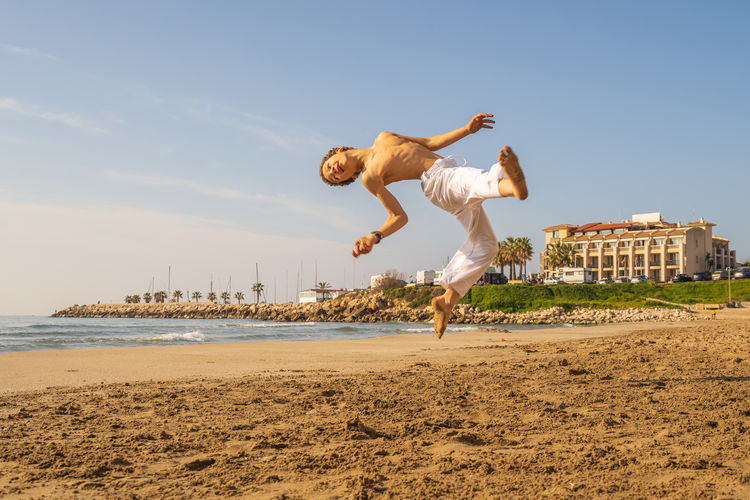 Man jumping on beach against sky