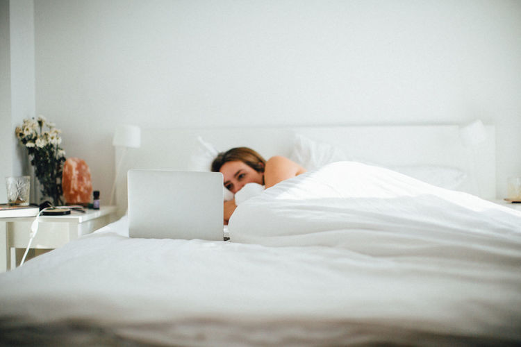 Woman using laptop while lying on bed at home
