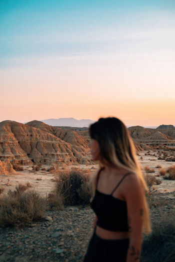Positive female traveler standing in dry valley in bardenas reales and enjoying sunset in summer while looking away