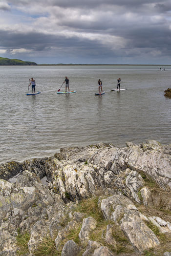 People paddleboarding in river against cloudy sky