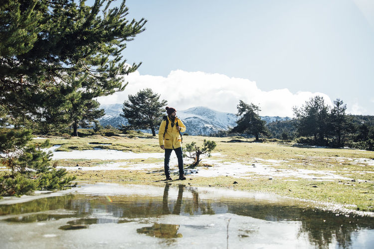Young man with yellow jacket and backpack next to pond in the mountain