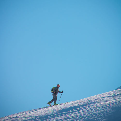 Low angle view of man walking on mountain against clear blue sky