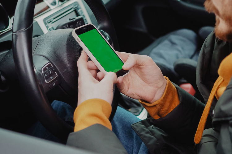 Midsection of man using mobile phone while driving car