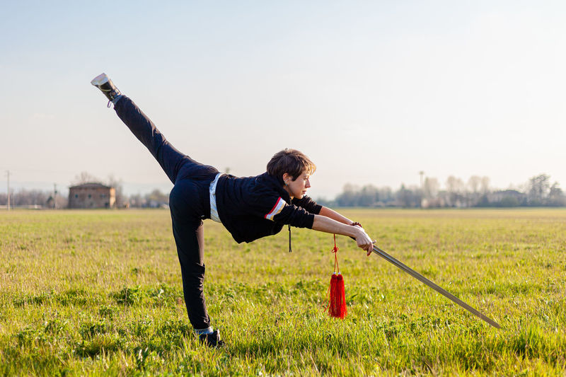 Caucasian young woman practicing wushu martial art on a green meadow with a sword