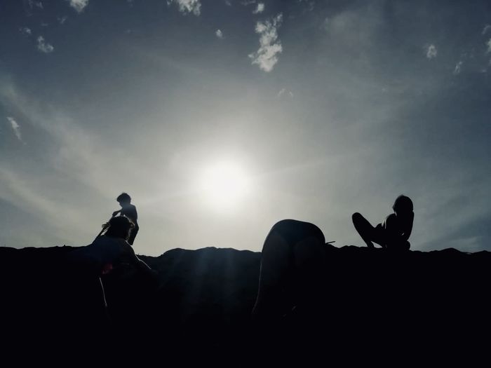 Silhouette men sitting on land against sky