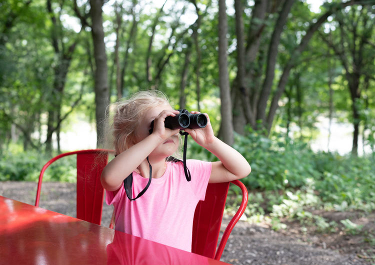Close-up of girl looking through binoculars at table in forest