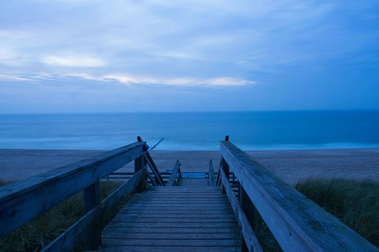Empty wooden pier on sea against sky
