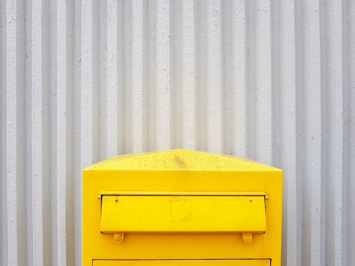 Yellow mailbox against corrugated iron