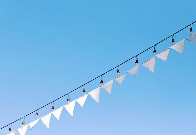 Low angle view of buntings and lighting equipment against clear blue sky