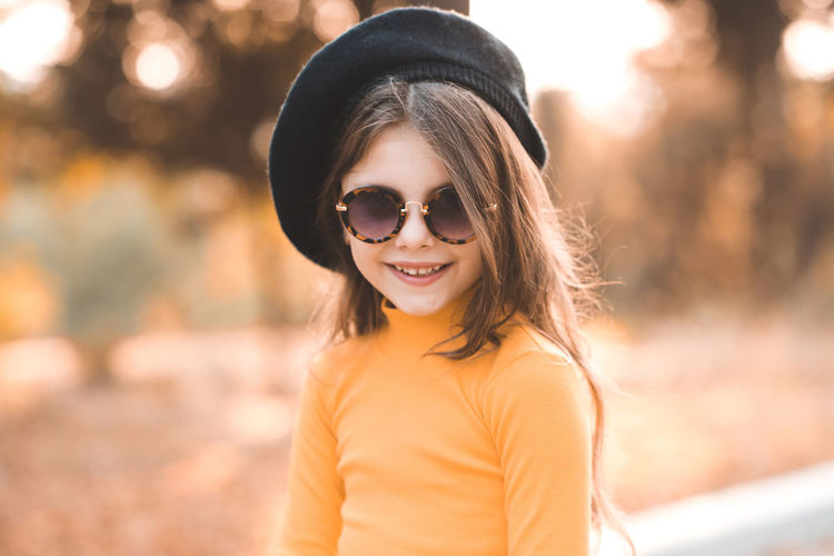 Funny cute kid girl 4-5 year old wear sun glasses and yellow knitted dress posing background