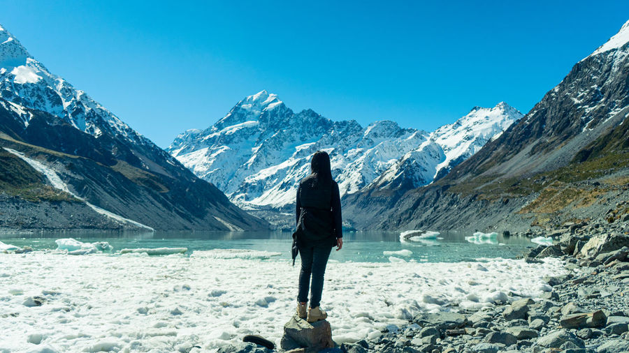 Rear view of woman standing on snowcapped mountain against sky