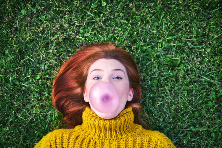 Portrait of woman blowing bubble gum while lying on grassy land