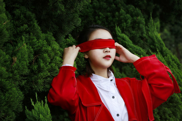 Young woman covering eyes with red strap against plants