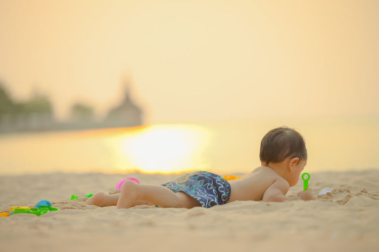 Baby boy on beach against sky during sunset