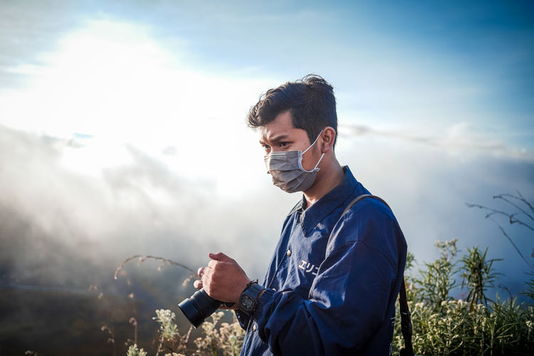 Young man wearing mask with camera standing on mountain