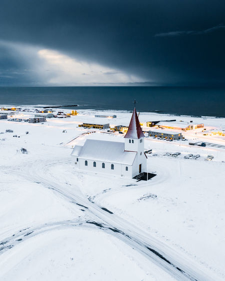 Scenic view of snow covered building by sea against sky