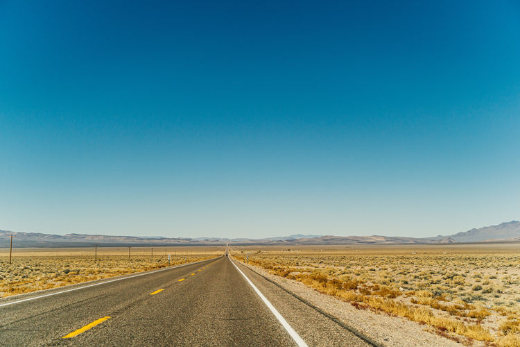Empty road along landscape against clear blue sky