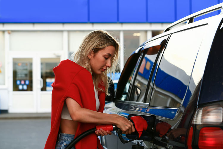 Young woman refueling her car at a gas station. attractive blonde female student. blurred selective 