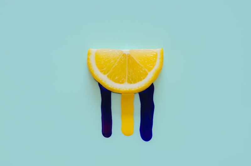 Slice lemon that have poster color drop from it with blue background. minimal summer concept.