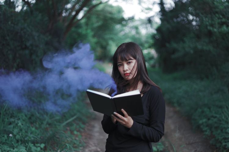 Portrait of woman holding book while standing in forest