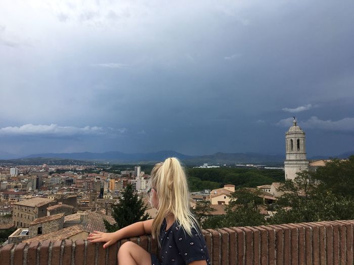 Side view of girl looking at cityscape against cloudy sky